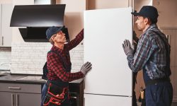 Moving again. Young men mechanics moving refrigerator Moving again. Young men mechanics moving refrigerator